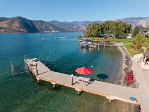 A clear lake with a dock extending into the water, a red umbrella, and a row of red chairs. - The Red Lake House | Beach & Dock Access (Chelan)