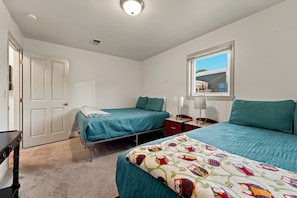 A bedroom with two beds, a window, a bedside table with a lamp, and a door. - The Red Lake House | Beach & Dock Access (Chelan)