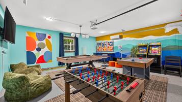 Een kamer met een tafelvoetbaltafel, een pooltafel en een televisie.