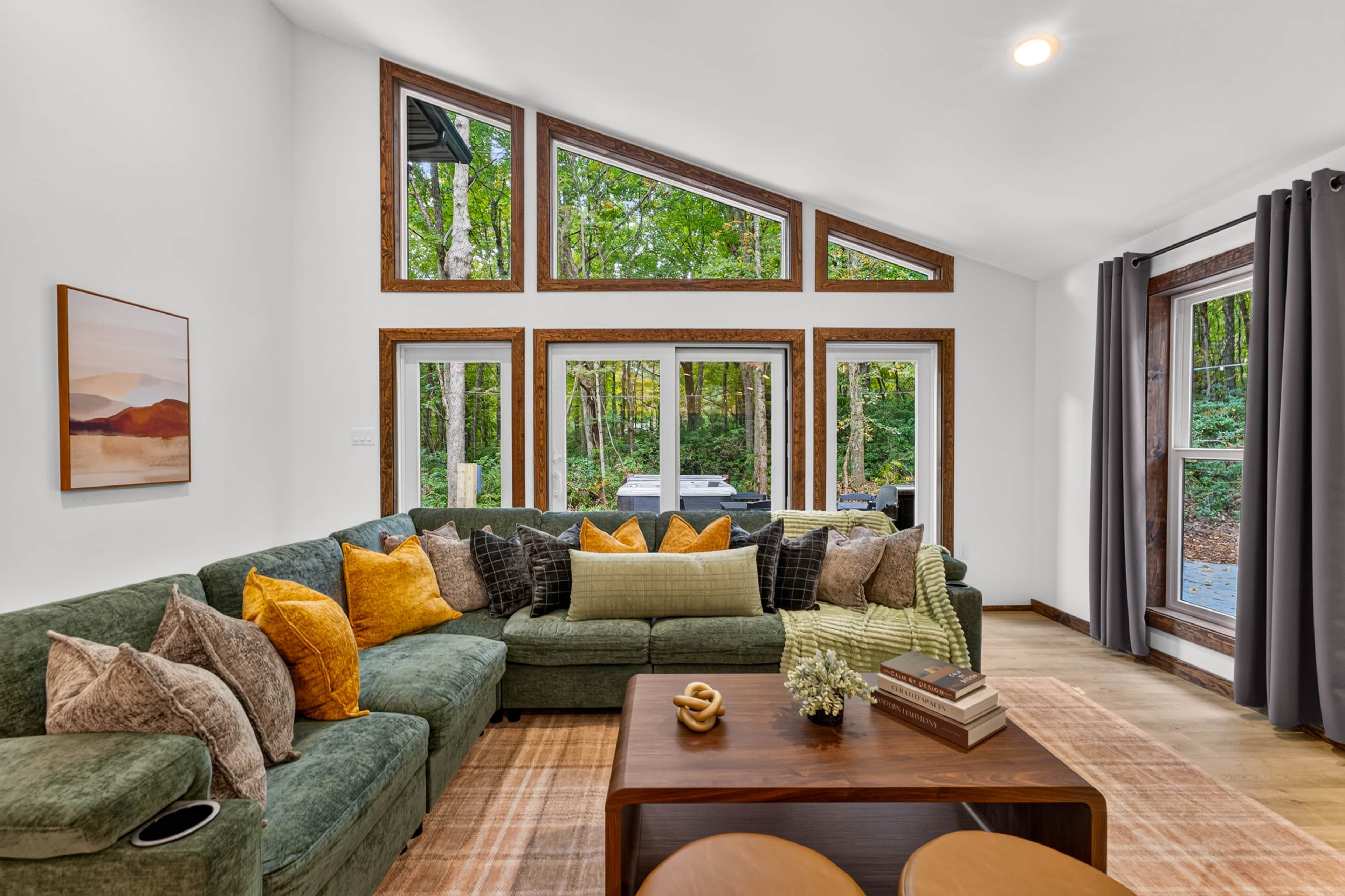 Una sala moderna con un sofá modular, una mesa de centro y ventanas amplias con marcos de madera.
