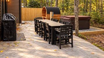 Eine Außenpatio mit einem Holztisch und -stühlen, einem Grill und einer überdachten Sitzgelegenheit.
