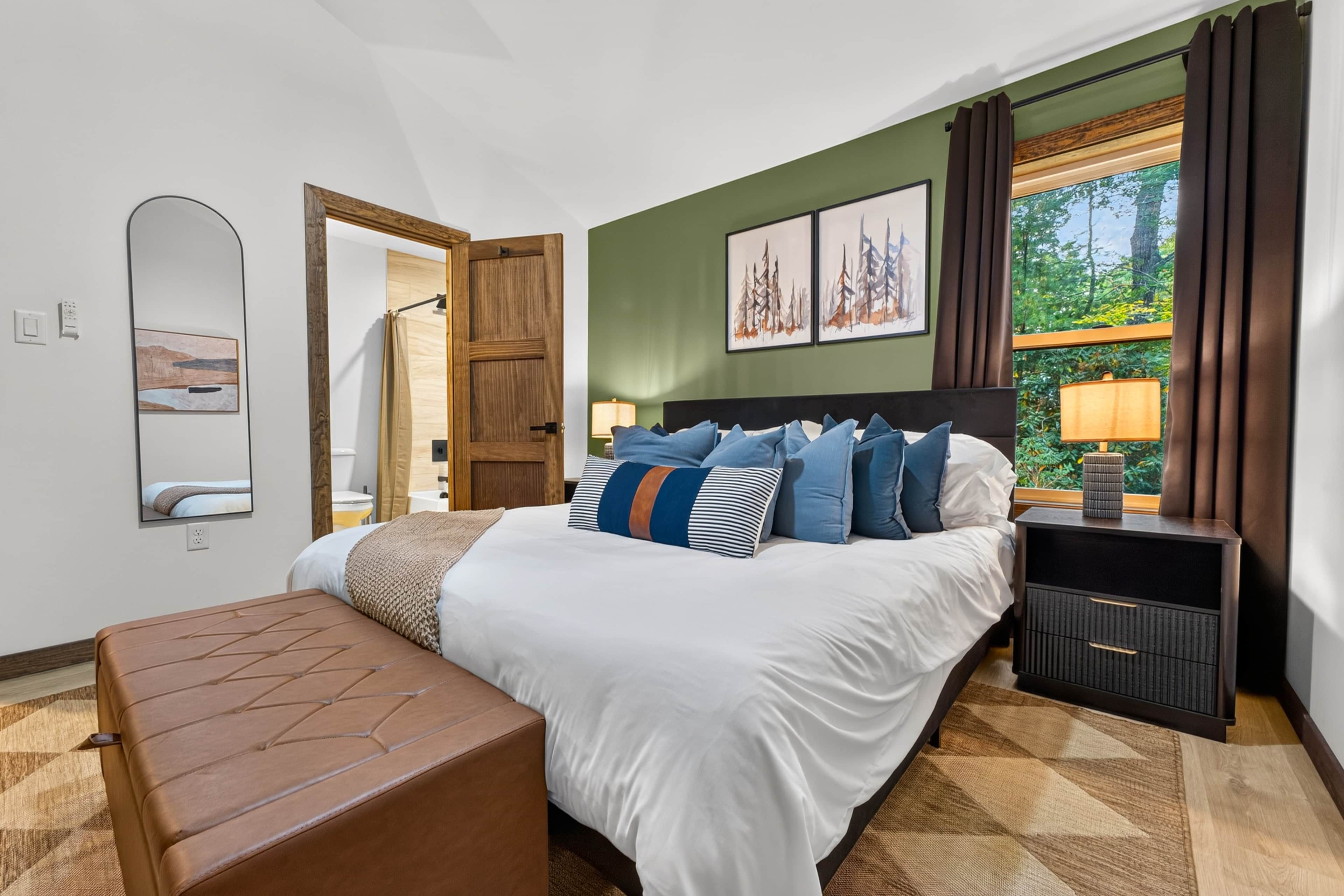 A hotel room with a large bed, bedside tables, a bench, a mirror, and artwork on the walls.