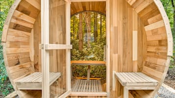 A wooden sauna with a bench and a window, surrounded by trees.