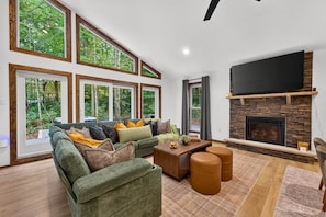 Una sala de estar moderna con un sofá grande, una chimenea y amplias ventanas con vistas al exterior.