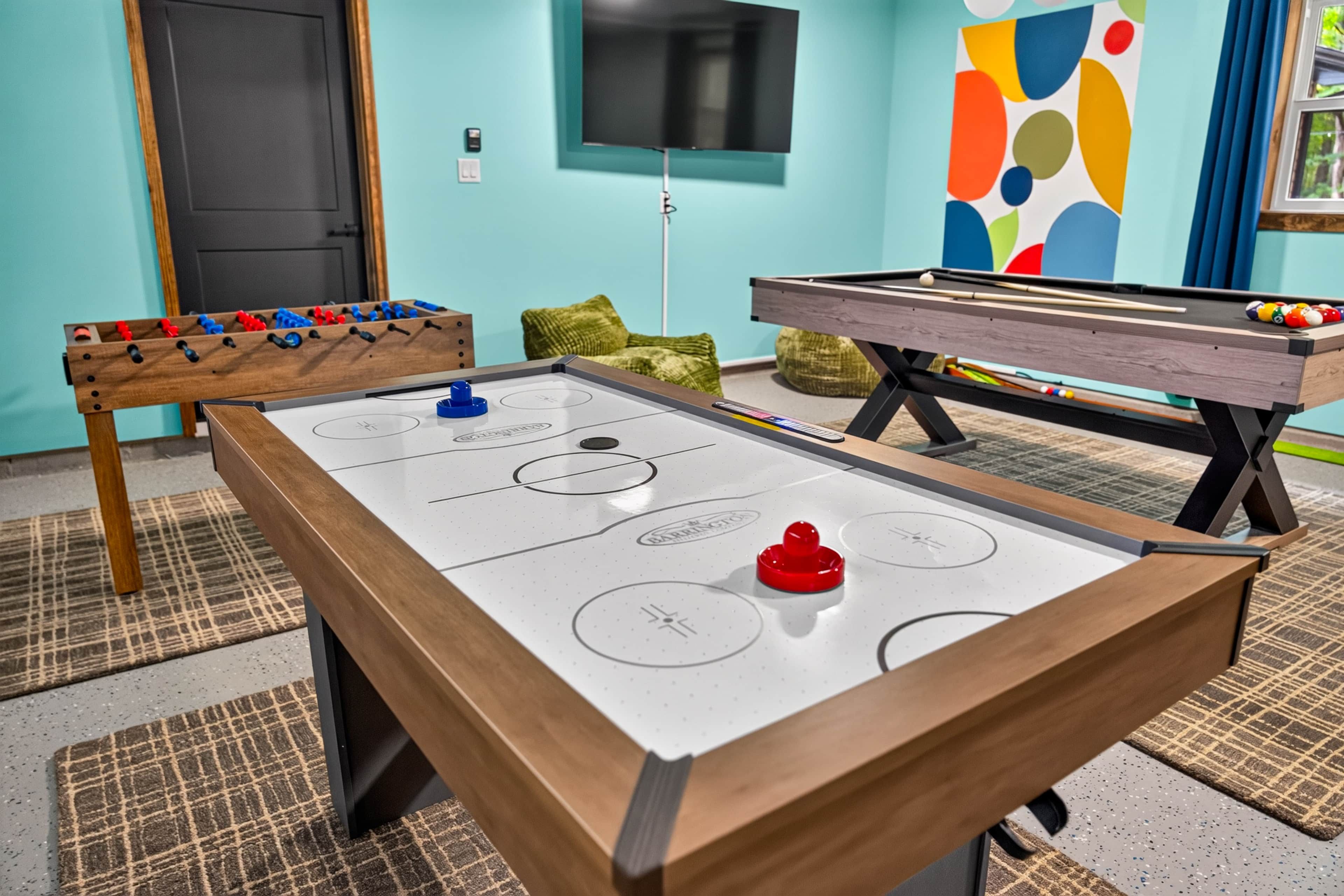 A pool table with a red puck in the center, a foosball table to the left, and a billiards table to the right.