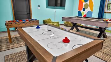 A pool table with a red puck in the center, a foosball table to the left, and a billiards table to the right.