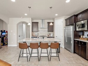 Una cocina moderna con una isla central, taburetes de bar, electrodomésticos de acero inoxidable e iluminación colgante.
