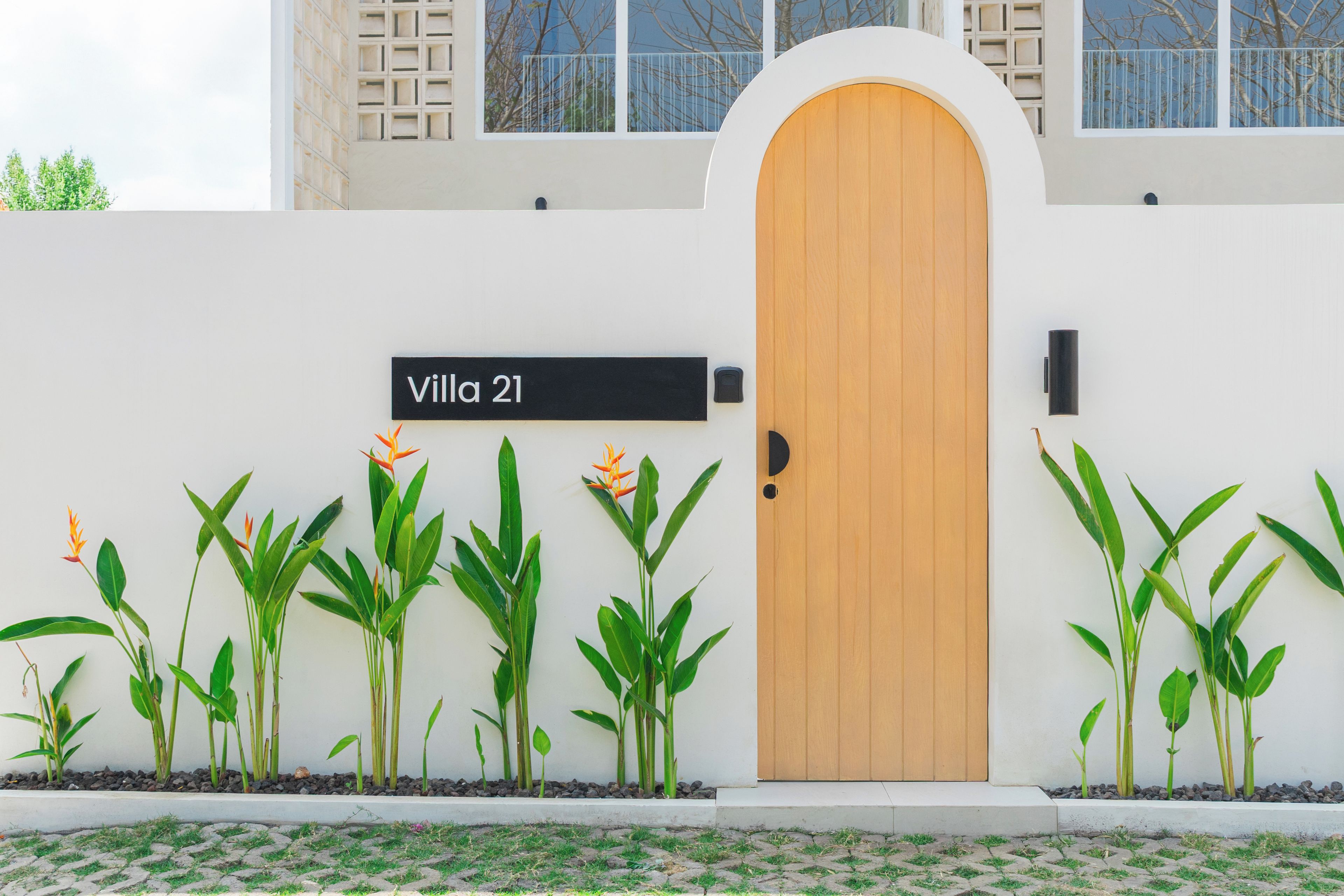 Una villa con una puerta de madera, un cartel que dice 'Villa 21' y una fila de plantas al frente.