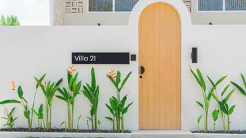 Una villa con una puerta de madera, un cartel que dice 'Villa 21' y una fila de plantas al frente.