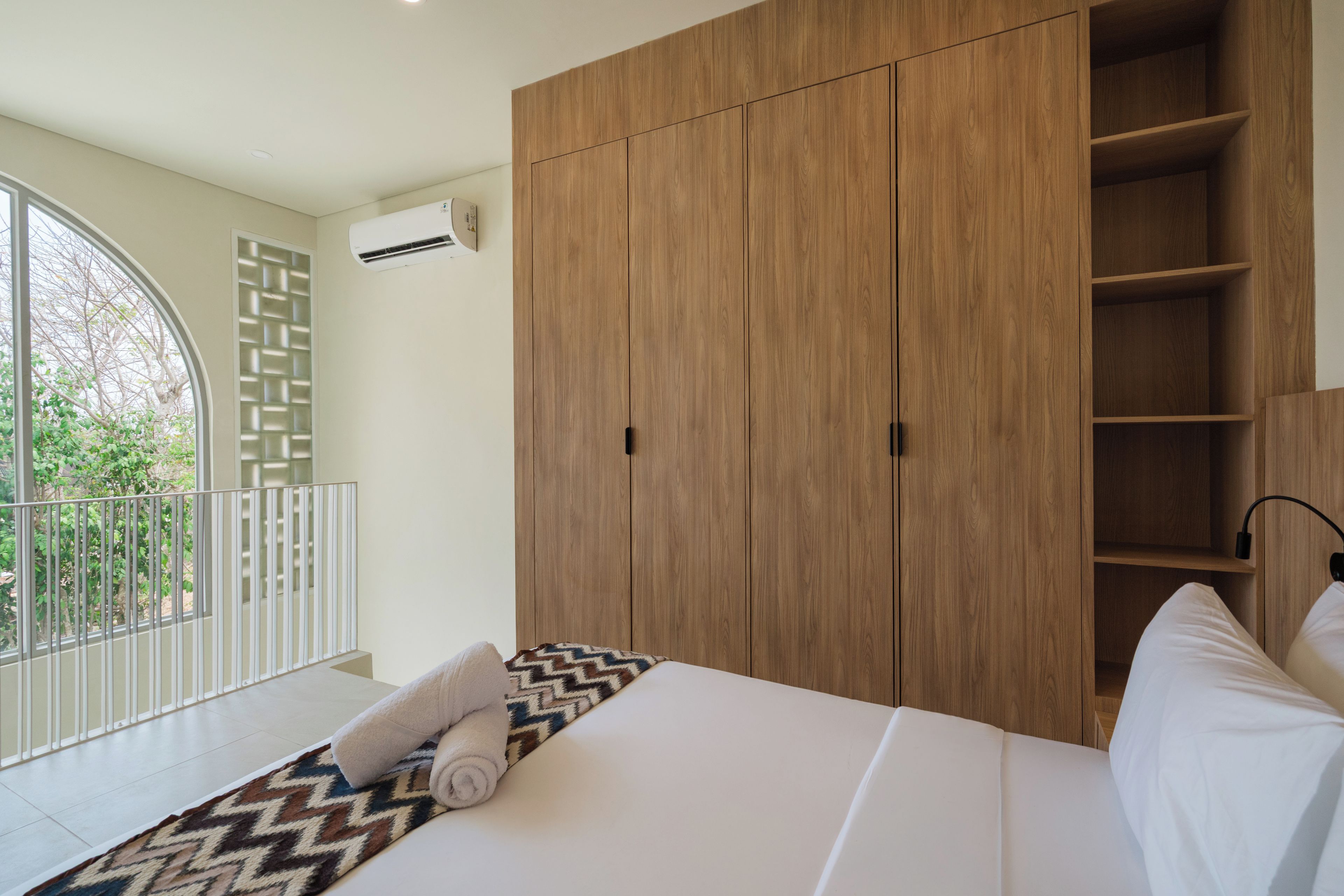 Un dormitorio con cama, armario, balcón con barandilla y aire acondicionado.