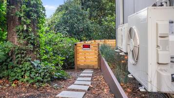 Uma trilha estreita leva a um portão de madeira com a inscrição 'PRIVATE PROPERTY', cercada por vegetação exuberante e uma unidade externa branca.