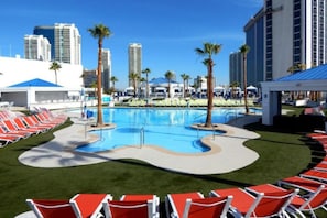 A swimming pool with red lounge chairs and palm trees, surrounded by high-rise buildings. - New Year’s Eve in Las Vegas — Stay on the Strip (Las Vegas)