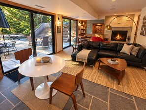 Ein modernes Wohnzimmer mit Kamin, einer Ledersofa, einem Esstisch und Blick auf eine Holzterrasse.