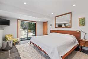 Ein Schlafzimmer mit einem großen Bett, einem Flachbildfernseher, einem hölzernen Kopfteil, einem Nachttisch mit Lampe und einem großen Spiegel.