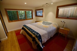 Ein Schlafzimmer mit einem Bett, einem Nachttisch, einer Lampe und zwei Fenstern.