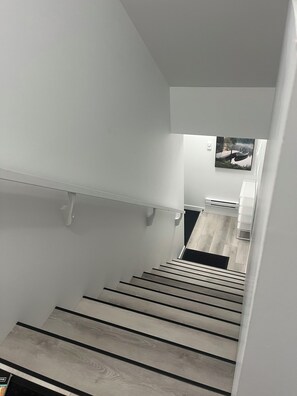 Eine moderne Treppe mit Holzvertäfelung und schwarzen Sprossen, die zu einer Zwischenebene mit einer weißen Wand und einem gerahmten Bild führt.