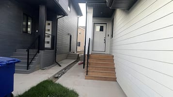 A residential building with a front door, a staircase, and a blue trash bin.