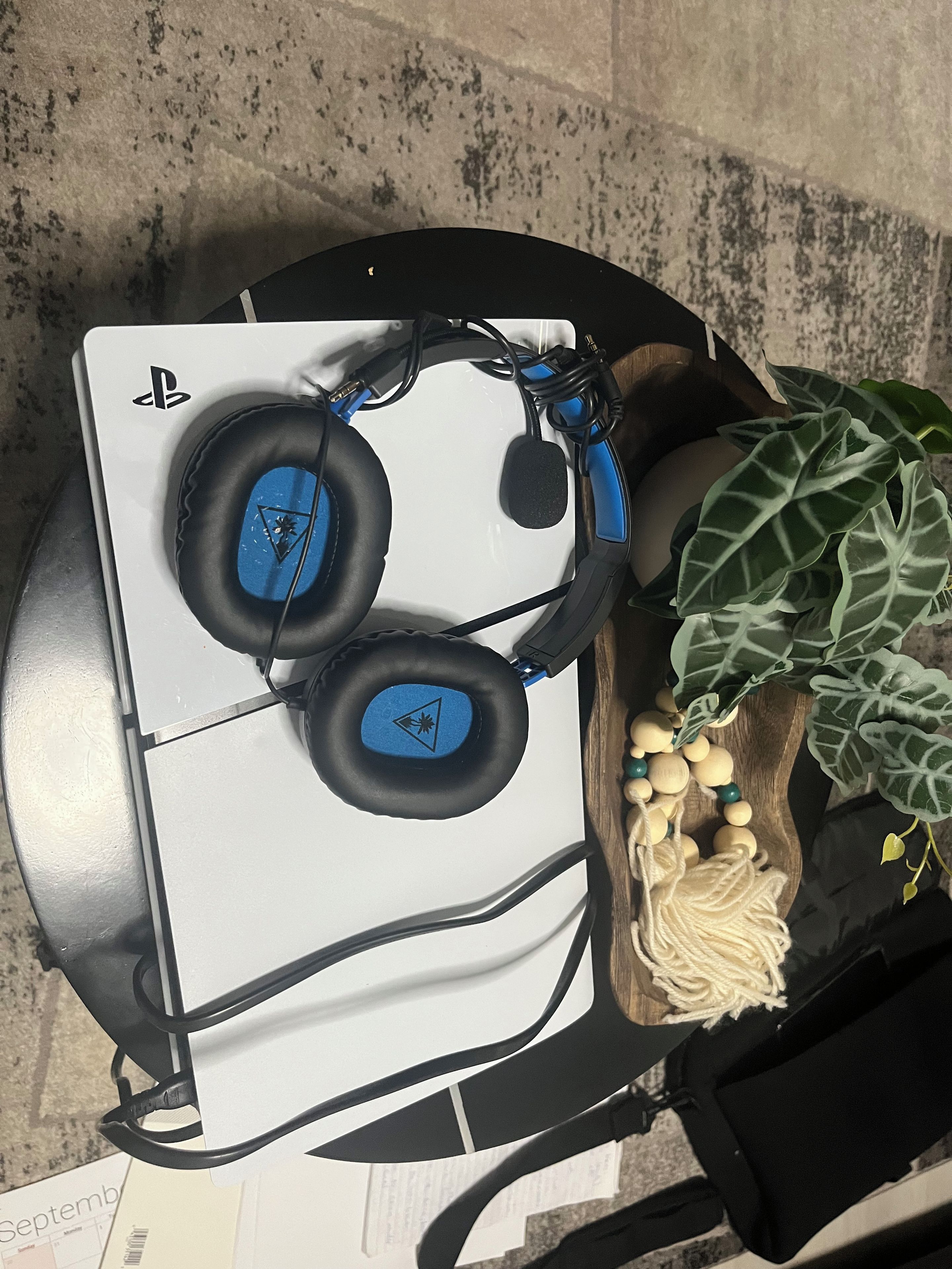 A white gaming console with headphones, a wooden plant stand, and a decorative item with beads.