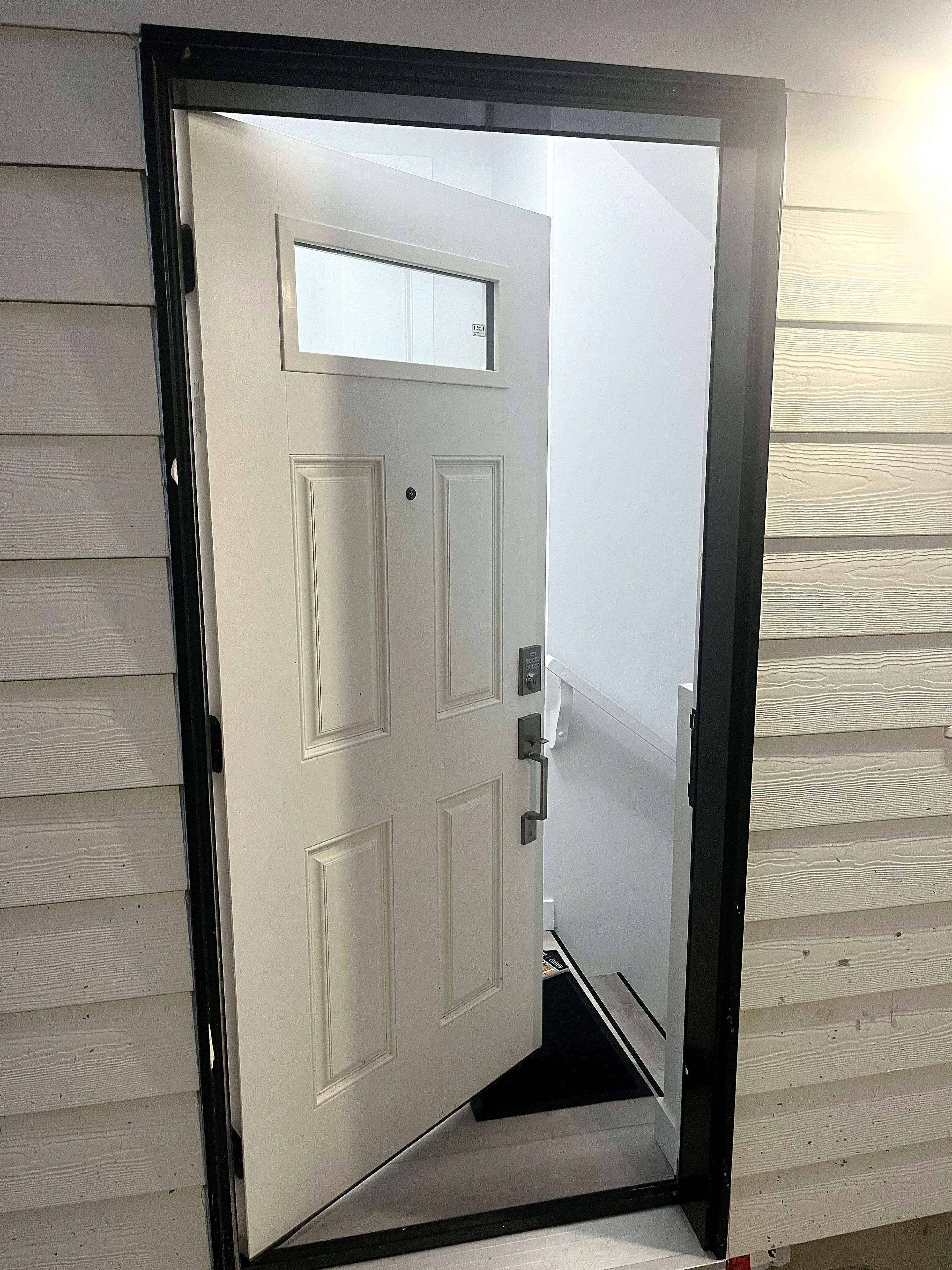 Une porte blanche avec un cadre noir, une petite fenêtre au-dessus et un sonnette.