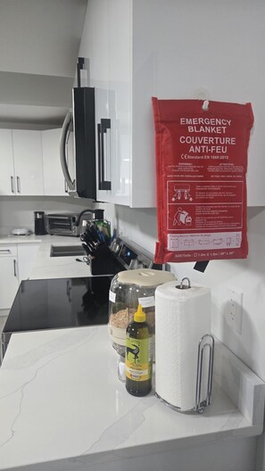 Eine Küchenarbeitsplatte mit weißer Marmoroberfläche, eine Olivenölflasche, eine Rolle Küchenpapier und eine rote Notfalldecke, die an der Wand hängt.