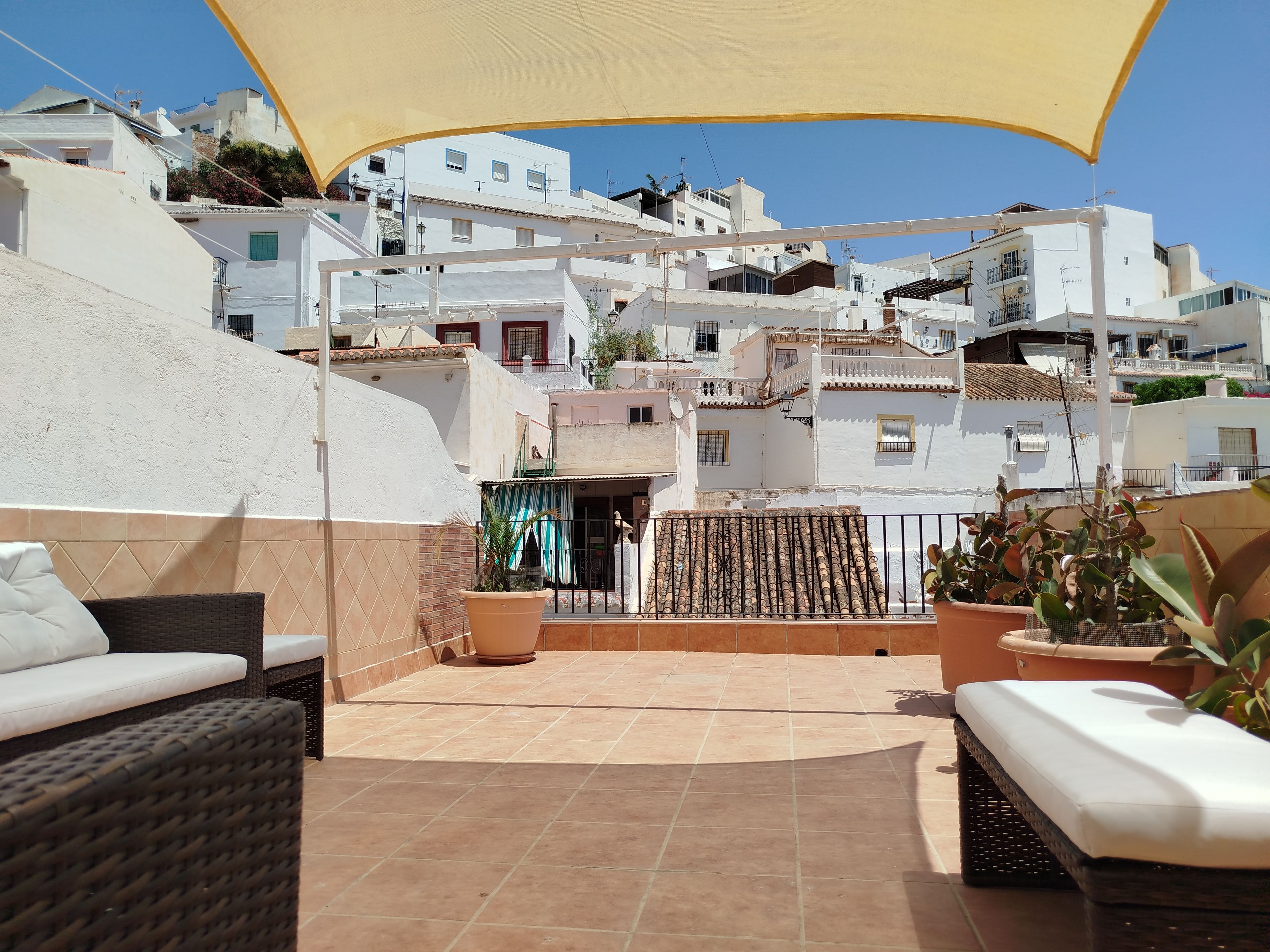 Une terrasse dotée de meubles en osier, de plantes en pot et offrant une vue sur des bâtiments blancs.