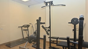Un gimnasio con equipo de ejercicio, incluyendo una cinta de correr, banco de pesas y diferentes estaciones de levantamiento de pesas.