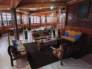 A spacious indoor area with wooden furniture, including sofas and chairs, and a dining area with tables and chairs.