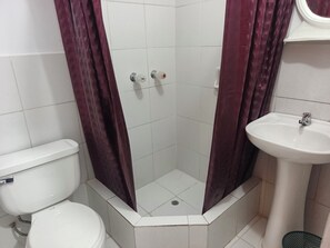 Um banheiro com vaso sanitário branco, chuveiro com porta de vidro e pia branca.