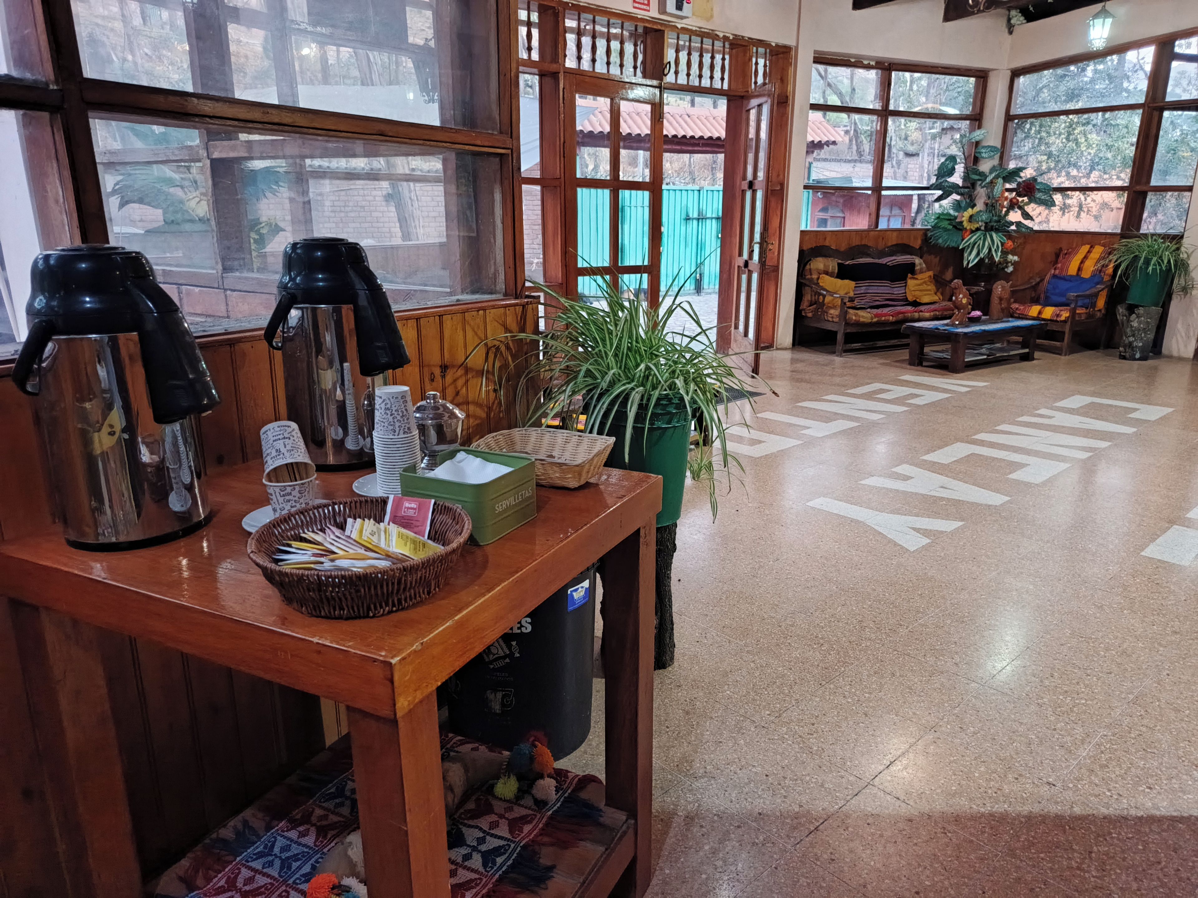 A wooden table with a coffee maker, cups, and a basket of utensils.