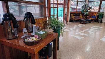A wooden table with a coffee maker, cups, and a basket of utensils.