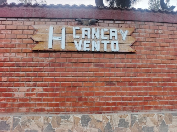 A brick wall with a wooden sign that reads 'CANELA VENTO'.