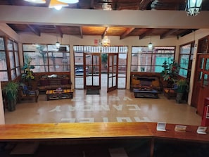 A reception area with a wooden bench, a sofa, and a coffee table. There are potted plants and a chandelier.