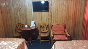 Ein Zimmer mit zwei Betten, einem an der Wand befestigten Fernseher, einem Tisch mit Wasserkocher und Tassen sowie zwei Stühlen.