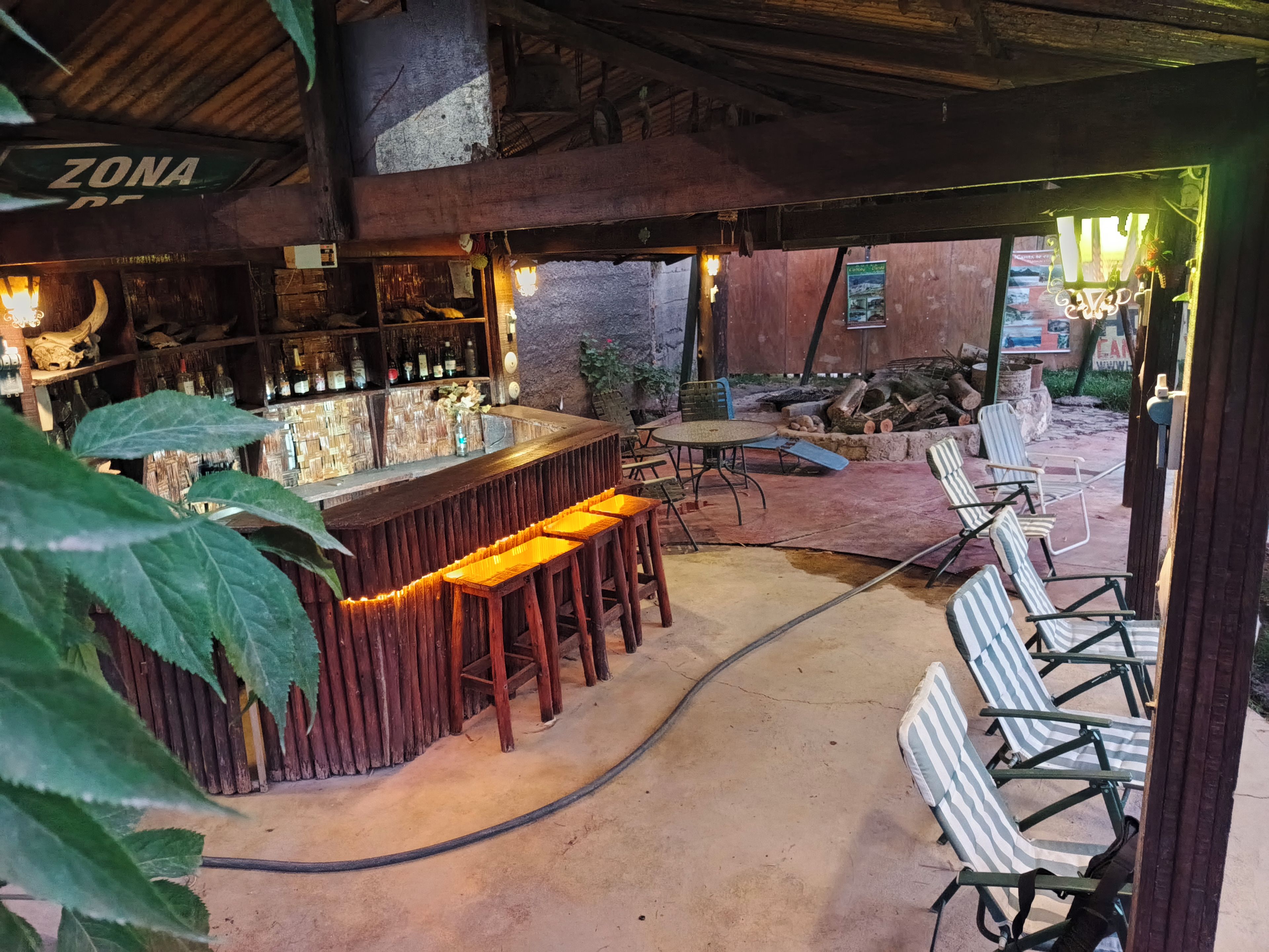 A rustic bar area with wooden stools, a bar counter, and a seating area with striped chairs.