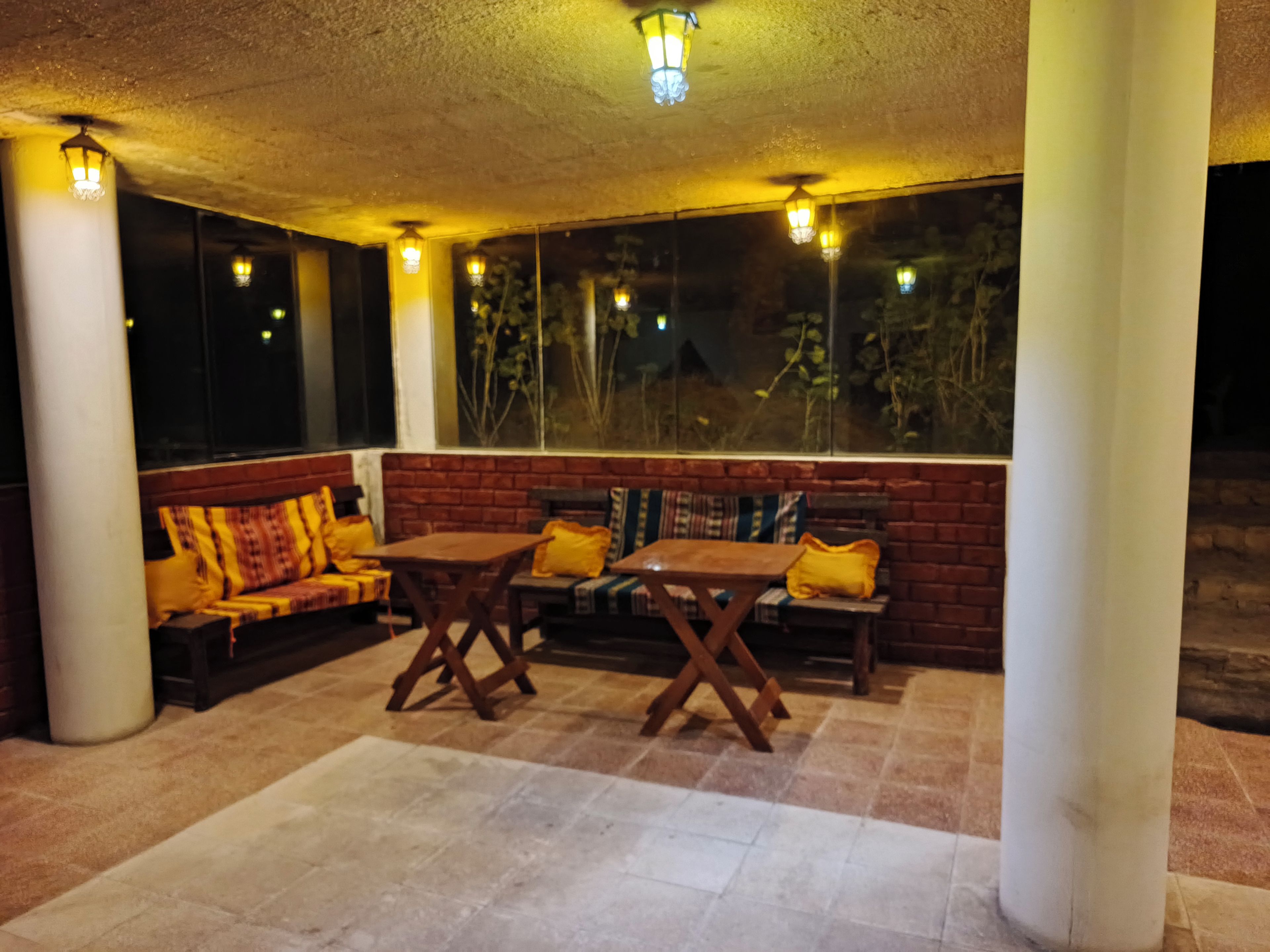 An outdoor seating area with wooden tables and benches, surrounded by large windows and columns.