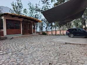 A building with a stone-paved entrance, a car parked in front, and a large canopy overhead. - Hotel Cancay Vento  (Canta)