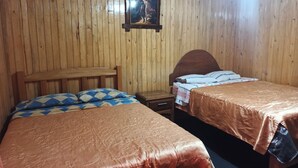 Ein Zimmer mit zwei Holzbetten, einer Holzbank, einem Nachttisch und einem gerahmten Bild an der Wand.