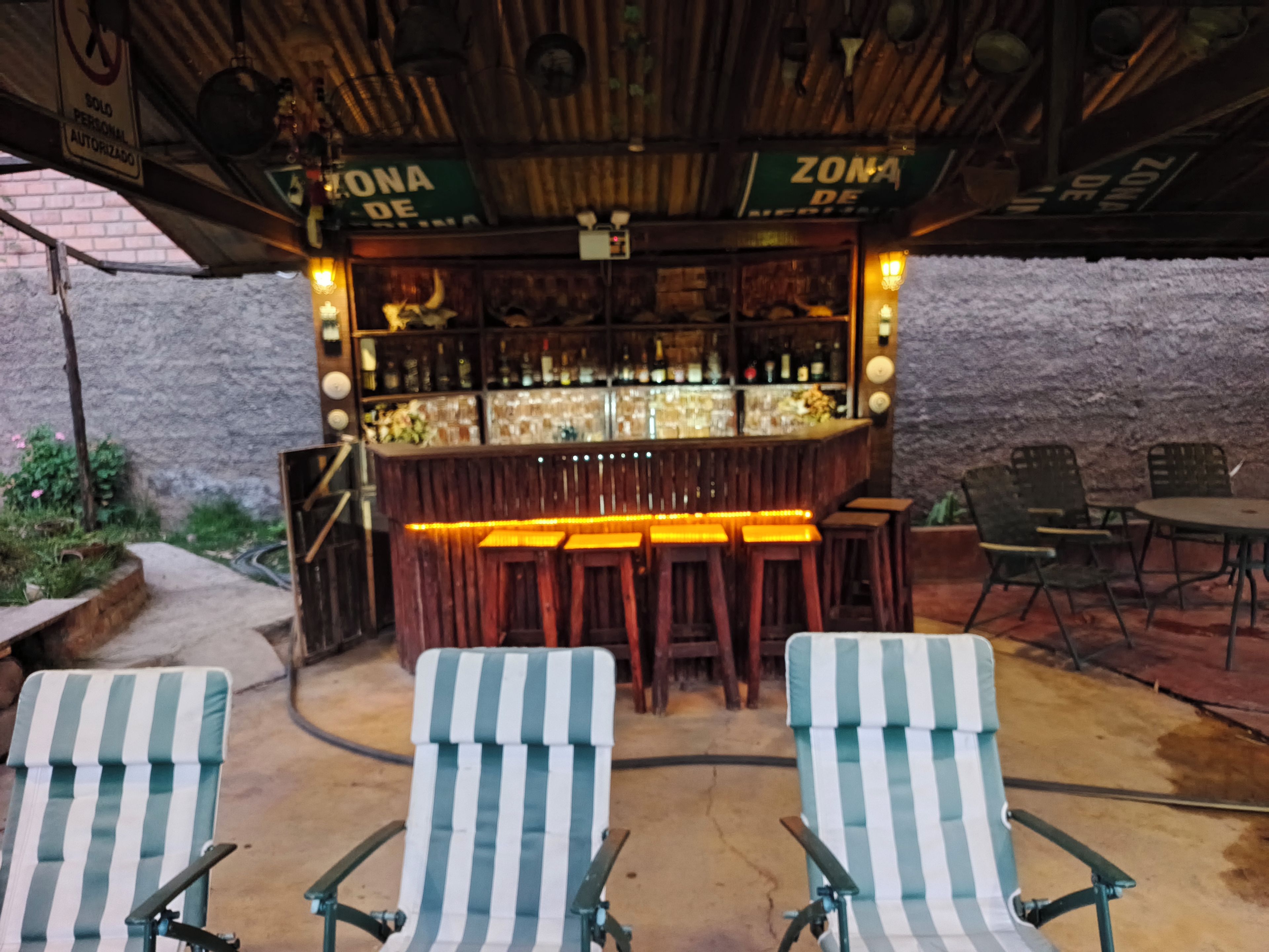 An outdoor bar area with a rustic wooden ceiling, bar stools, and a seating area with striped chairs.