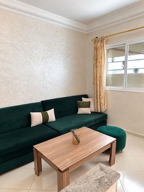 A living room with a green sofa, a wooden coffee table, and a marble accent table.