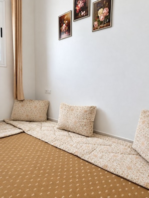 A room with a sofa set against a white wall, a patterned rug, and three framed floral paintings.
