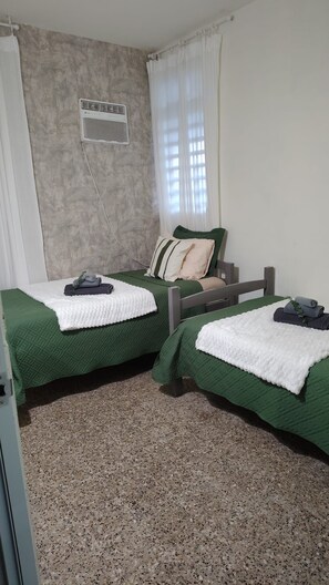 A room with two beds, a window with curtains, a wall-mounted air conditioner, and a textured floor. - San Juan: Cerca de aeropuerto, playas y zonas turísticas - 3 hab. 2 baños (San Juan)