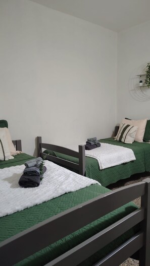 Ein Zimmer mit zwei Einzelbetten, jeweils mit grüner Bettdecke und weißen Kissen, sowie einer weißen Decke auf dem Boden.