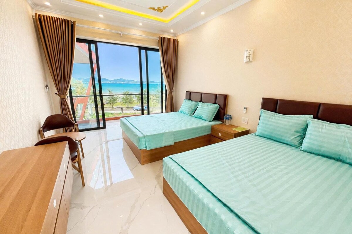 A hotel room with two beds, a desk, and a view of the sea.