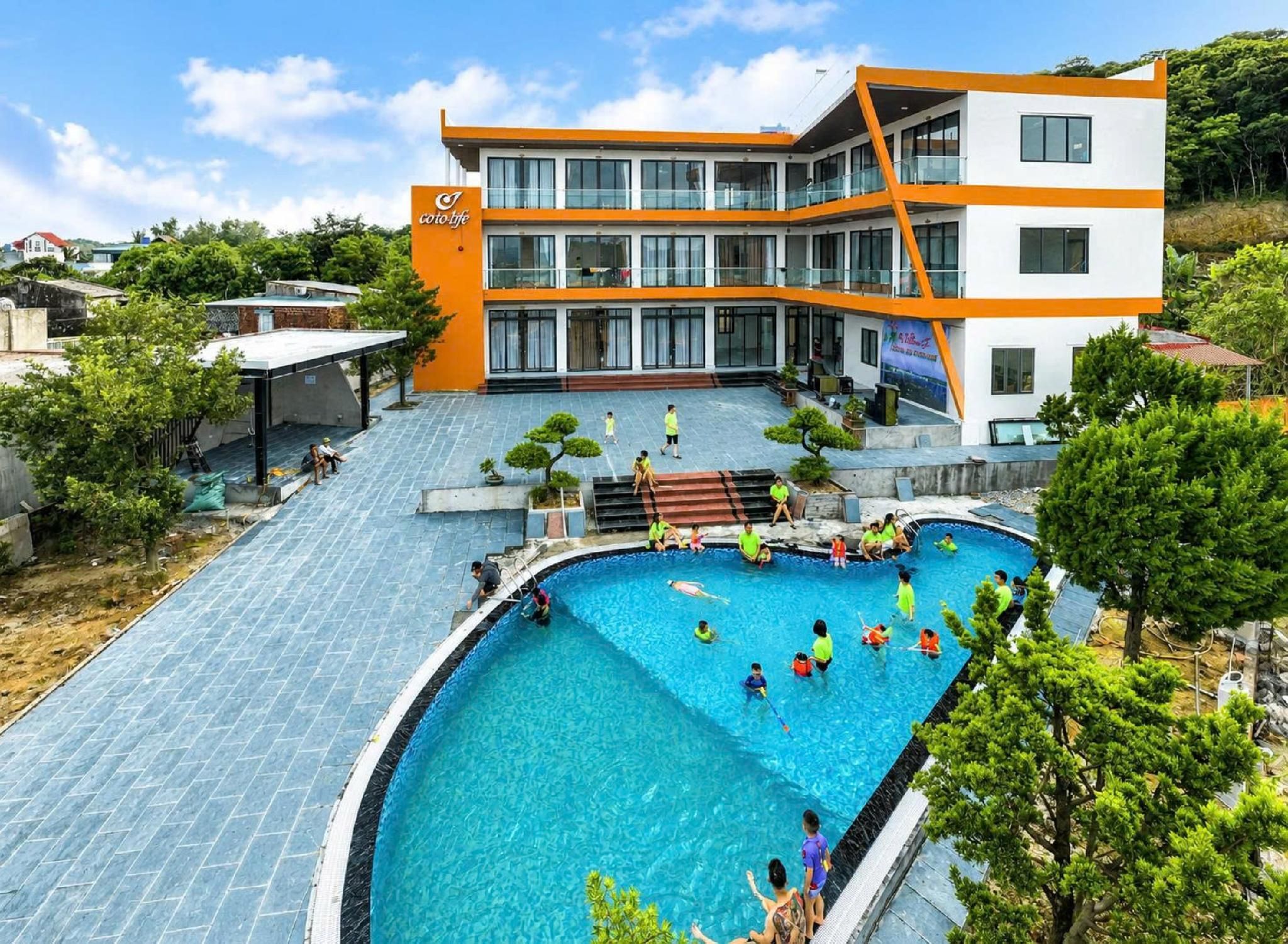 A swimming pool with people around it, a building with orange and white exterior, and a clear sky.
