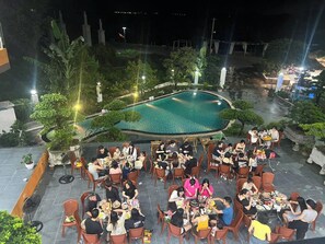 An outdoor dining area with a pool, surrounded by greenery and stone structures.