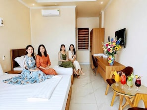 A hotel room with a bed, a desk, a TV, and a dining table with drinks.