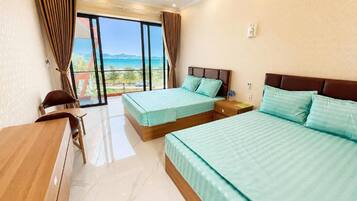 A hotel room with two beds, a desk, and a view of the sea.