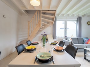 Ein Essbereich mit Tisch für vier Personen, eine Treppe und ein Wohnzimmer mit einer Couch.