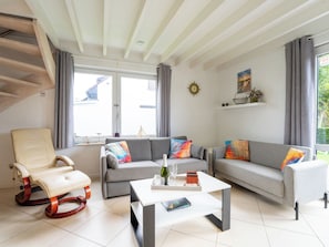 Ein modernes Wohnzimmer mit einer Couch, einem Sessel und einem Couchtisch, einer Treppe und einem großen Fenster mit Vorhängen.