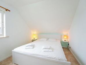 A single-bed room with a sloped ceiling, white bedding, two bedside lamps, and a window with blinds. - Ter Heide I with terrace & parking by Interhome (Westende-Bad)